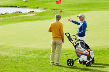 Obraz premium Two active senior man discussing small pond on play field while one of them pointing at it