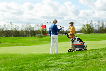 Two contemporary golf players in casualwear standing on new play field and discussing place for outdoor game