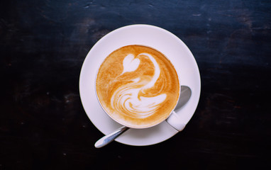 White cup of cappuccino with white swan drawn on brown coffee foam. Elegant coffee art. Concept background of cafe, rest, leisure, and romantic settings. View from above. Lomography hipsterish effect