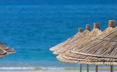 Close-up of reed beach umbrellas on a turquoise warm sea background. Text space.