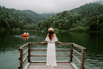 The woman with hat and white dress standing against lake in nature.
