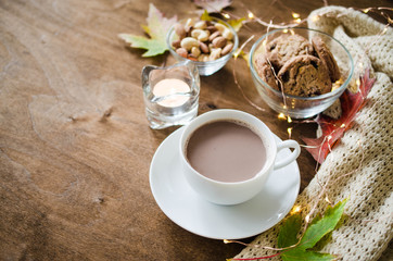 A cup of hot cocoa, nuts, cookies, candle and knitted plaid on a rustic wooden table.