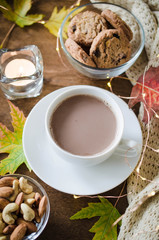 A cup of hot cocoa, nuts, cookies, candle and knitted plaid on a rustic wooden table.