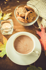 A cup of hot cocoa, nuts, cookies, candle and knitted plaid on a rustic wooden table.