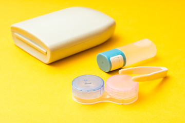 Accessories for storing lenses: a bottle of liquid, container, tweezers and case on a yellow background