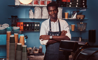 Portrait of a handsome African barista at counter of a trendy coffee shop.