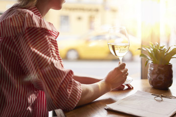 Woman in red dress drinking white wine near window in cafe, sunshine, chilling on vacation or holidays, bar concept.