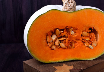 Half of a pumpkin with orange flesh on a wooden board surrounded by dry maple leaves