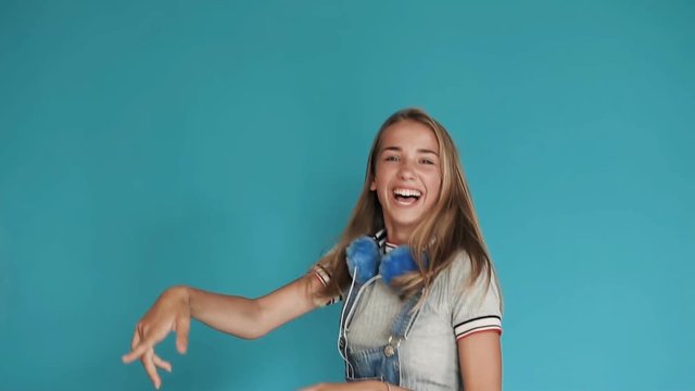 A little girl with big white teeth dancing on a blue background. Teen girl with bright, bright blue headphones, rejoices and jump near beautiful wall. Joy, smile and emotions.