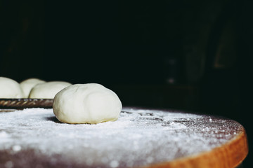 Raw dough ball on the wooden table covered by wheat powder. Homemade pizza preparation process