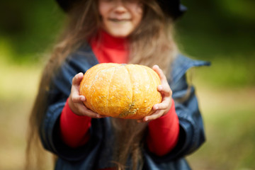 Ripe orange pumpkin in hands of little girl in halloween attire standing outdoors