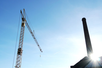 metal crane for construction and silhouette pipe of industrial factory with blue sky background