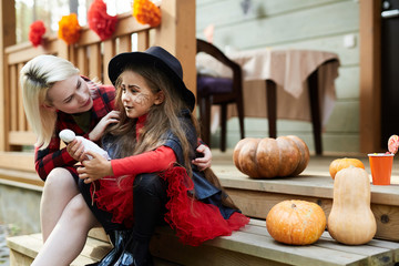 Young mother embracing her little girl in halloween attire while both sitting by terrace of country house
