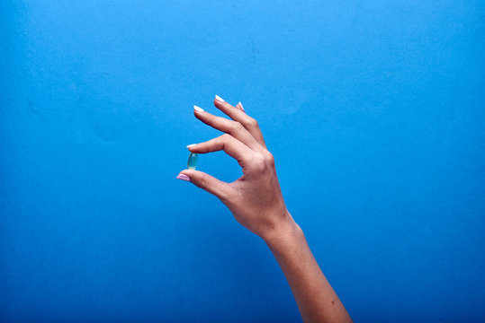 A woman holds a transparent fish oil capsule, a useful source of omega-3. Treatment with dietary supplements, vitamins and minerals. Pharmaceutical advertising in the style of minimalism.