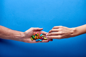 A woman's hand takes a small jelly candy from a man. Many multi-colored drugs for therapeutic therapy against diseases in a sick patient. Yellow, purple, orange, red, blue, green, pink pills.