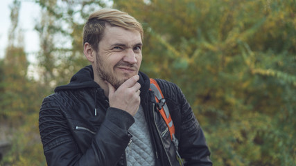 A handsome guy posing against the autumn nature. Blond in a leather jacket on the street