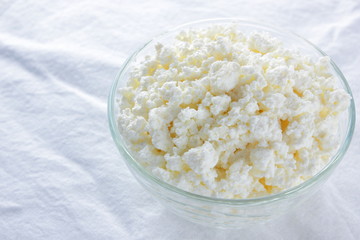 Cottage cheese. Cottage cheese on white background. Soft cheese in glassware on white napkin. Dairy product for breakfast. Copy space