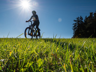 Fototapeta na wymiar Boy cycle with his bike down the hill on green grass and blue sky landscape