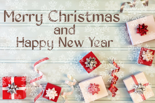 On a light blue background, small gift boxes with bows, decorative ribbons, Christmas composition. Next to the inscription Merry Christmas and Happy New Year. Lots of snowflakes in blur.