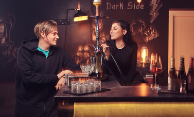 Seductive brunette womansmokes a hookah and handsome guy in hoodie.