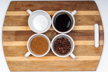assortment of four white cups of coffee on a saucer grain, instant, brewed and an empty cup on the wooden surface background
