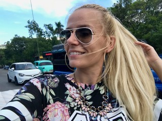 Beautiful young blonde European tourist woman happy smiling in a Cuban vintage retro car on a sunny day wearing sunglasses in Havana (La Habana), the capital of the Caribbean island of Cuba