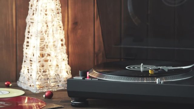 Christmas picture. The rotating moment of a black vinyl record on the turntable, the stylus with a needle falls on vinyl, music on the background of a glowing Christmas tree with red glass balls