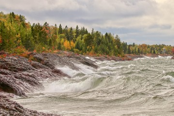 Wild stormy waves on rocky shore of Lake Superior along Autumn forest