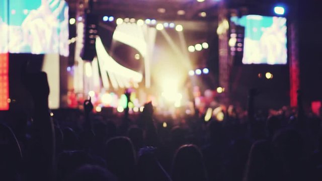 Slow motion silhouettes of fans at a music show, concert. Music festival of youth pop music. Laser show on the stage. A crowd of fans raised their hands, applause. Blurred background for your design