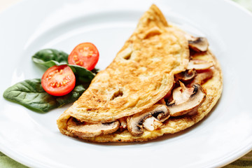 Omelet with mushrooms served on white plate with cherry tomatoes and spinach