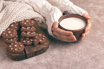 Female hands are holding cup of warm milk, chocolate cookies on the old wooden cutting board