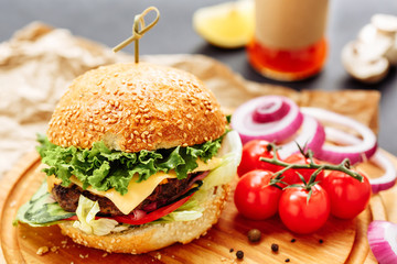 Fresh homemade burger on wooden board, pickles, sauce, cherry tomatoes and sliced onion. Side view, copy space