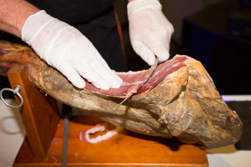 Knife cutting serrano  slicing of italian dry-cured ham prosciutto