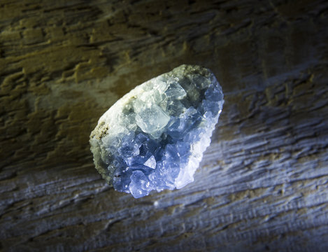 Raw celestine or celestite crystal cluster on wooden background, cool abstract side light.
