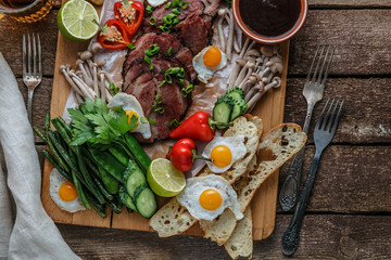 Breakfast meals variety flat lay. Top view on buffet wooden board with meat, eggs, vegetables, bread etc
