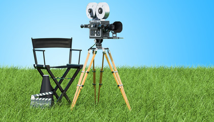 Obraz premium Cinema concept. Movie camera with film reels, chair, megaphone and clapperboard on the green grass against blue sky, 3D rendering