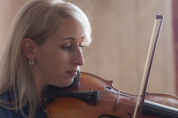 Young beautiful woman violin player looking at camera over instrument on her shoulder holding bow.