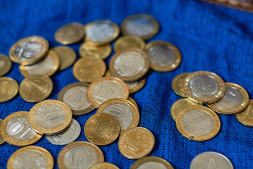 Money coins of various denominations and countries lie on a blue fabric background.