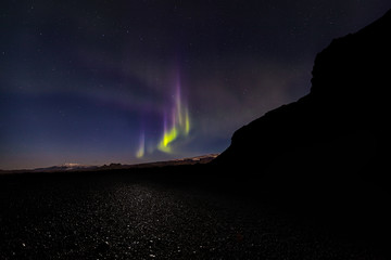 Aurora borealis over Reynisfjara black sand beach in Iceland as the moon lights up the glaciers in...