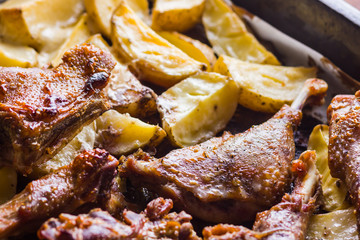 Baked meat with potatoes. Duck meat with golden crust on baking sheet. Cooked in oven dish on parchment. Golden sliced potatoes with chicken meat. Home kitchen