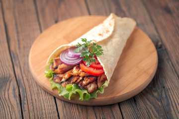 Doner kebab is lying on the cutting board. Shawarma with chicken meat, onions, salad lies on a dark old wooden table.
