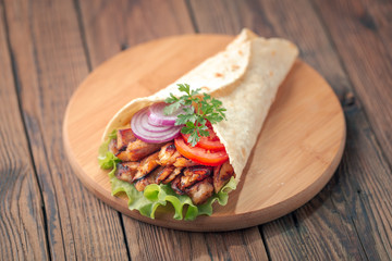 Doner kebab is lying on the cutting board. Shawarma with chicken meat, onions, salad lies on a dark old wooden table.