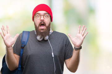 Young hipster man wearing red wool cap and backpack over isolated background celebrating crazy and amazed for success with arms raised and open eyes screaming excited. Winner concept