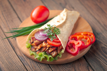 Doner kebab is lying on the cutting board. Shawarma with chicken meat, onions, salad lies on a dark old wooden table.