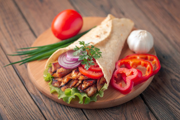 Doner kebab is lying on the cutting board. Shawarma with chicken meat, onions, salad lies on a dark old wooden table.