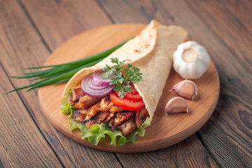 Doner kebab is lying on the cutting board. Shawarma with chicken meat, onions, salad lies on a dark old wooden table.