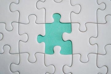 Fragment of a folded white jigsaw puzzle and a pile of uncombed puzzle elements against the background of a colored surface.