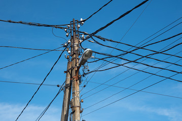 pole with electrical and telephone wires and a street lamp against a blue sky. internet cable....