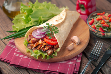 Doner kebab is lying on the cutting board. Shawarma with chicken meat, onions, salad lies on a dark old wooden table.