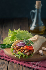 Doner kebab is lying on the cutting board. Shawarma with chicken meat, onions, salad lies on a dark old wooden table.
